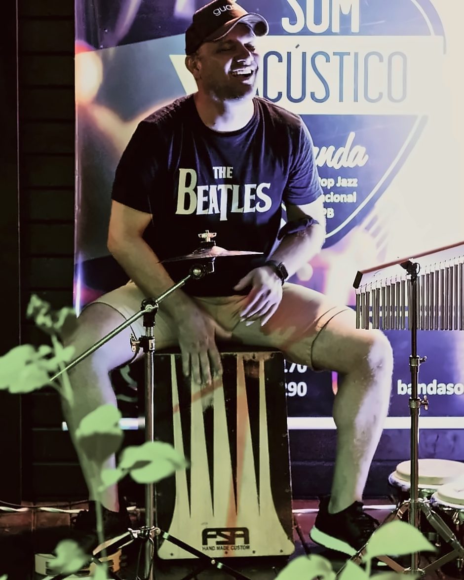 Robson rindo enquanto toca cajón, com camiseta dos Beatles